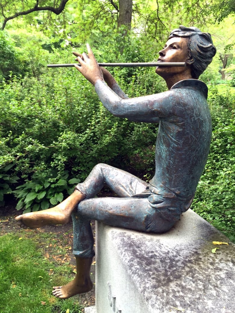Bronze statue of a boy seated playing flute with one leg crossed over another