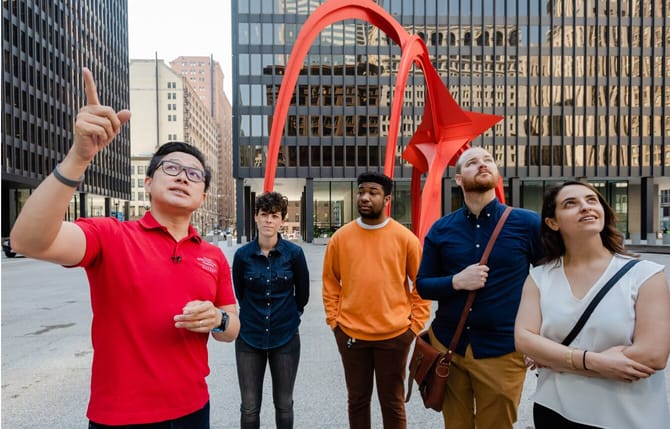5 People in an outside plaza with a red sculpture in the background. 