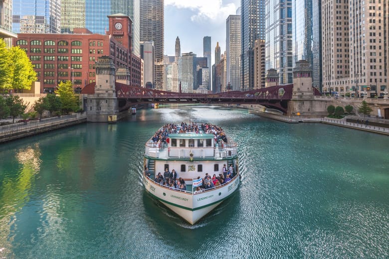 A large passenger boat going down the Chicago river with skyscrapers in the surroundings