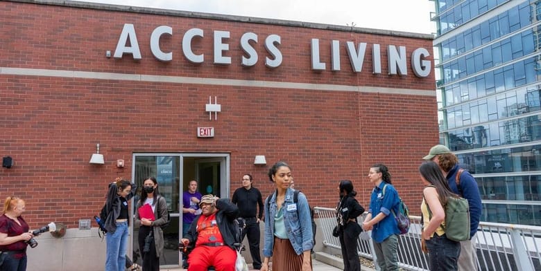 A group of people standing outside a brick building with Access Living name on the building