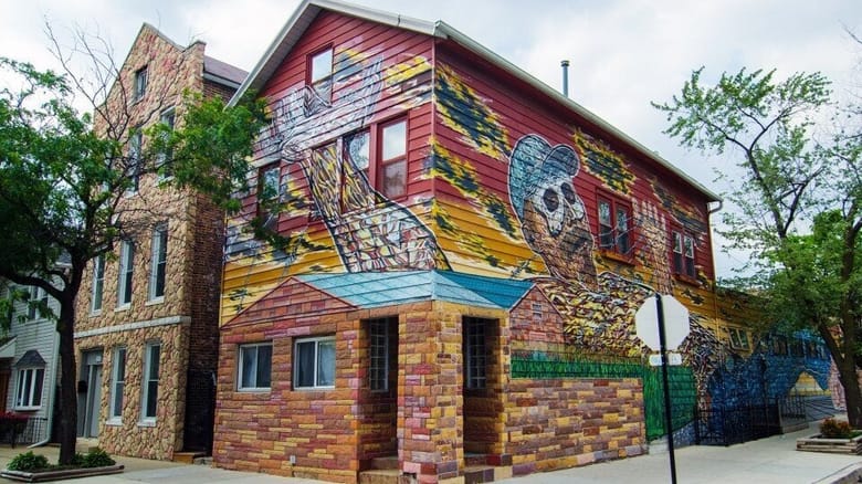 Exterior of brick and wood building with vibrant mural, on street corner.