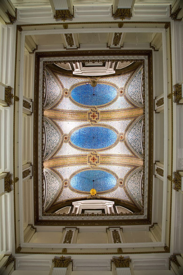 Image looking up at a mosaic ceiling with blue and tan tiles that is brightly lit.