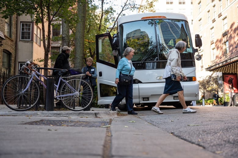 Image of two women walking in front of a white bus parked with the door open
