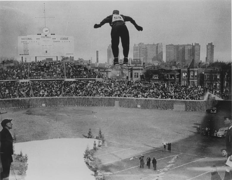 Black and white photo of a skier from behind in mid jump