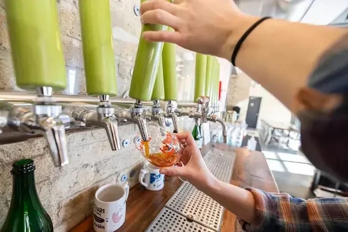 beer taps with green handles and arms that go out of frame pouring a glass of beer from one of the taps