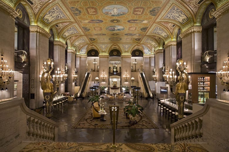 Hotel interior showing a painted ceiling, a staircase, and golden light fixtures and a Christmas tree in the center