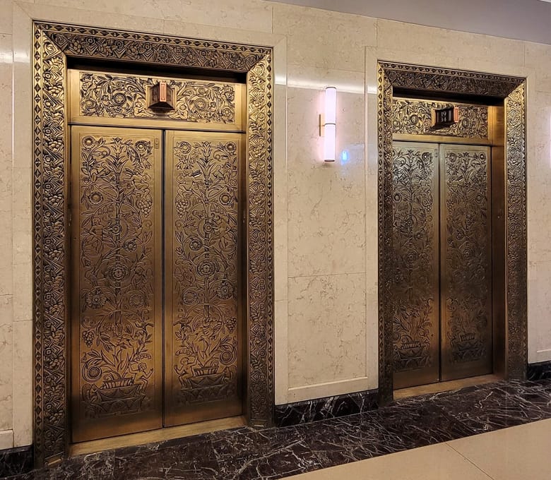 Two golden elevator doors that are ornately decorated in the art deco style.
