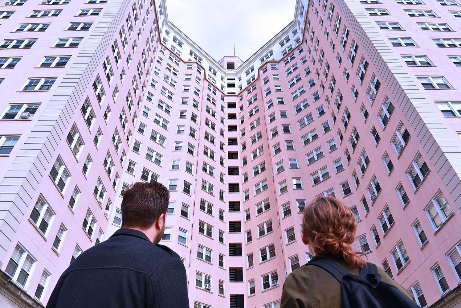 Shot from the back of a male and female looking onto a grand curved building in pink.