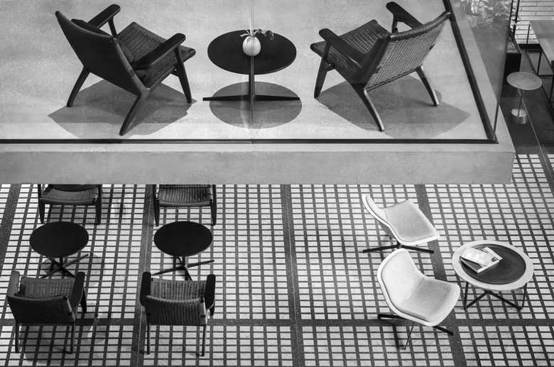 Black and white image looking down at a few sets of chairs and tables in mid-century style