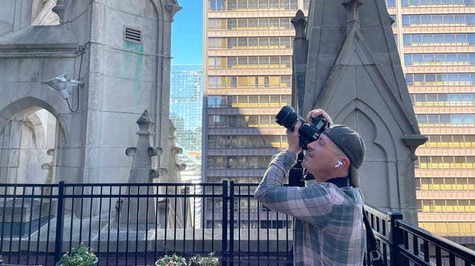 Man wearing a backwards baseball cap taking a photo of a building with a camera