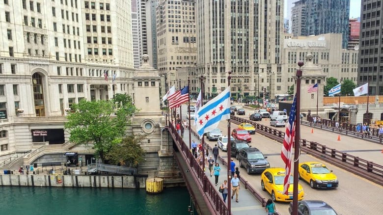 Bridge with cars, over river, with multiple flags. 