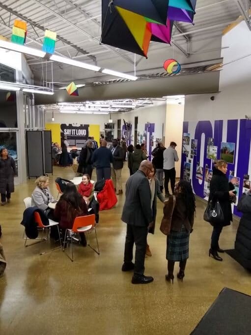 Gallery space with people standing and sitting talking to one another.