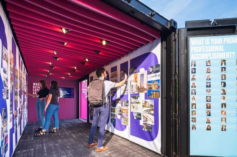 Gallery space with pink walls inside a shipping container with people inside looking at the walls.