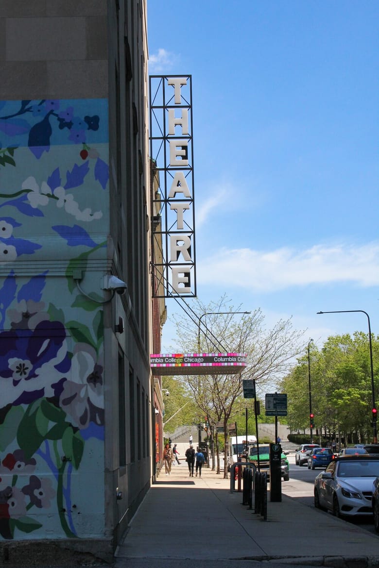 Side of a building with a floral mural and white sign on the side that reads "Theatre"