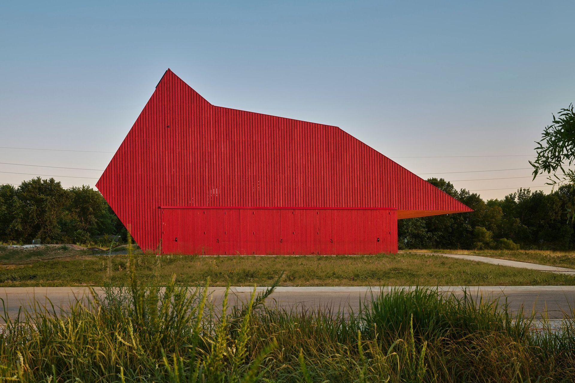 Large red angular building in the middle of a grassy field at dusk.