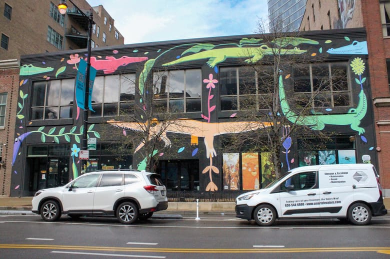Image of a two story black building with large windows and colorful alligators painted all over the facade.