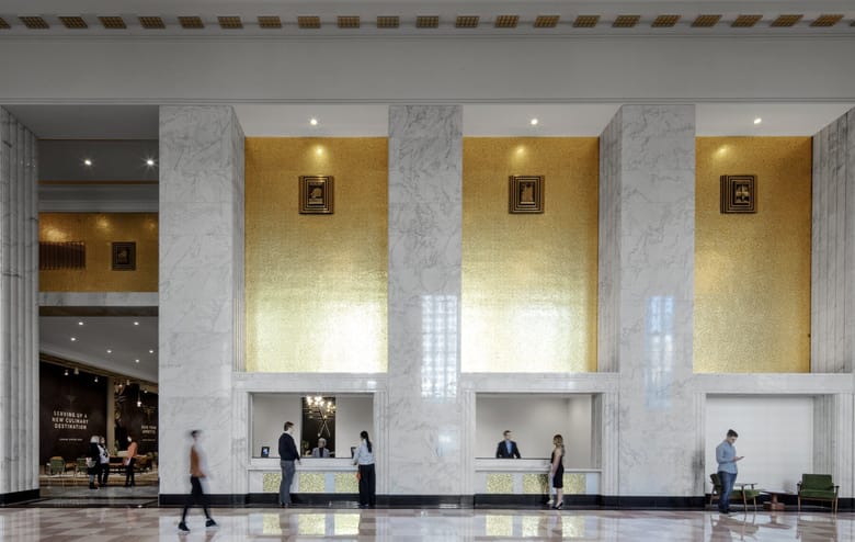 Image of a large hall with marbel colunmns and a lobby desk with gold walls behind it.