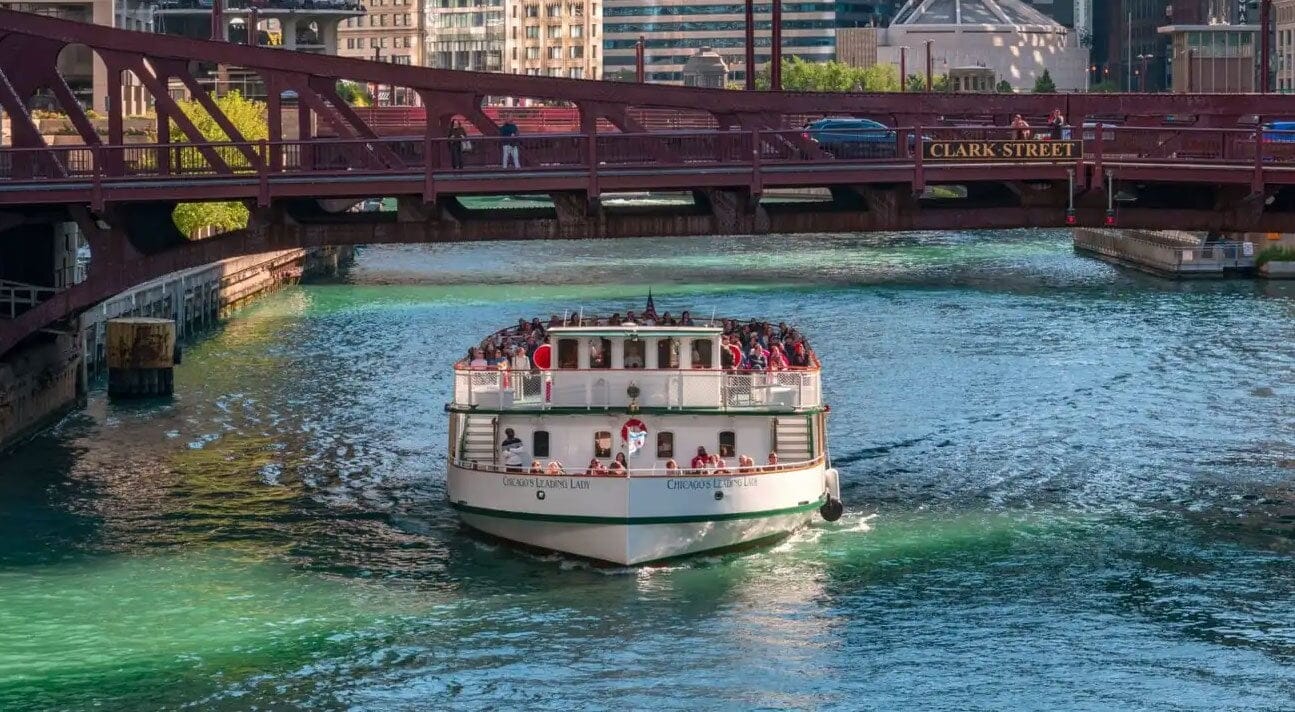A large passenger boat going down the Chicago river with skyscrapers in the surroundings