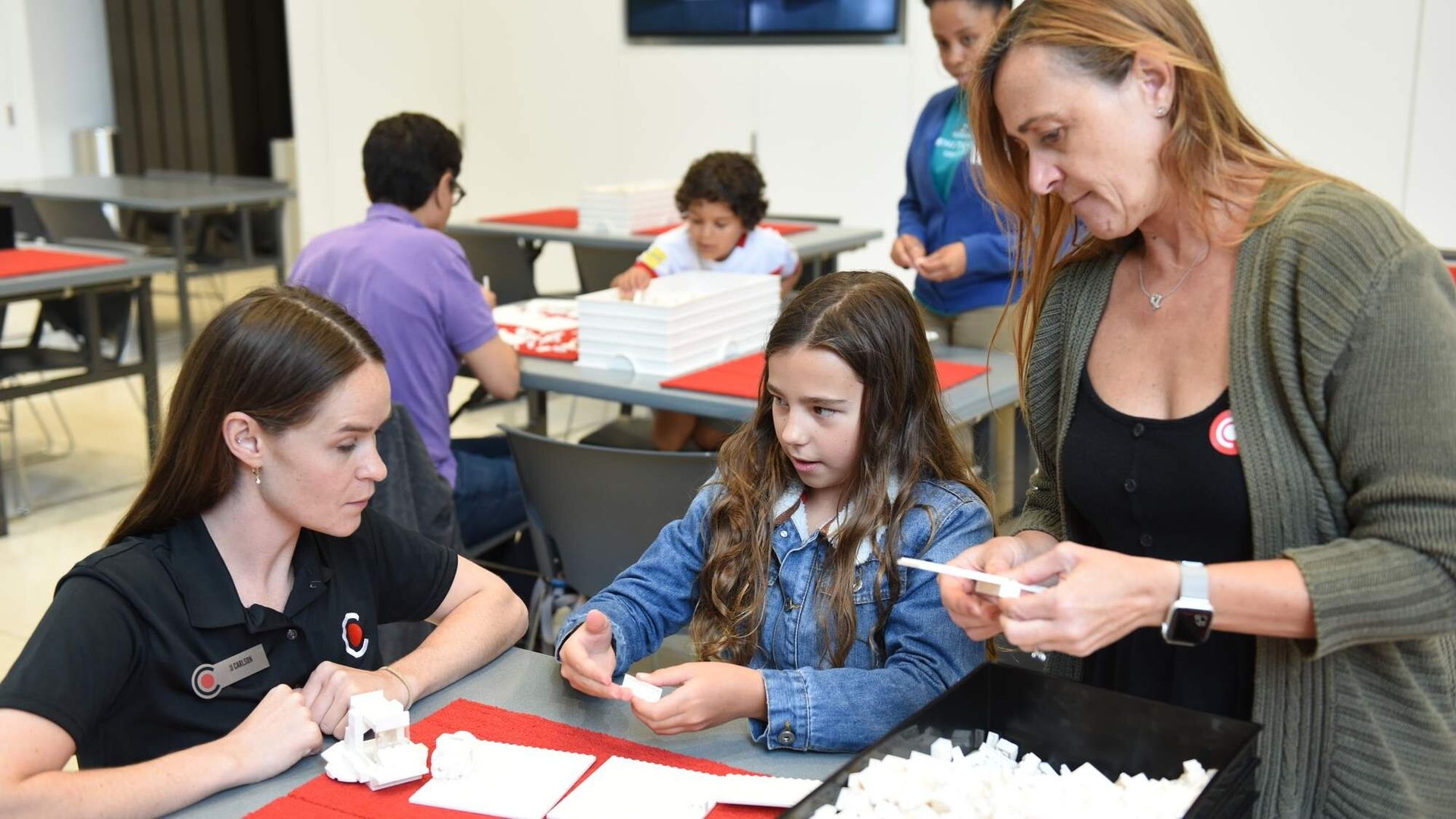 Two female adults looking on at a young girl as she explains to them about her project