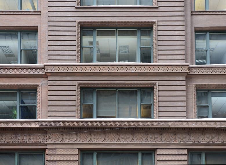 Close up image of the exterior of a brown building featuring the details of one of the windows including some relief carvings