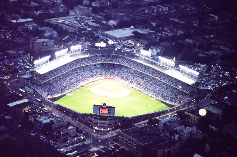 Aerial photo of Wrigley Field at night with lights on.