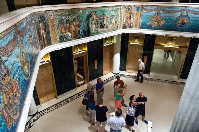 Interior shot of the lobby looking down from below with mosaics lining the walls and people in the lobby below